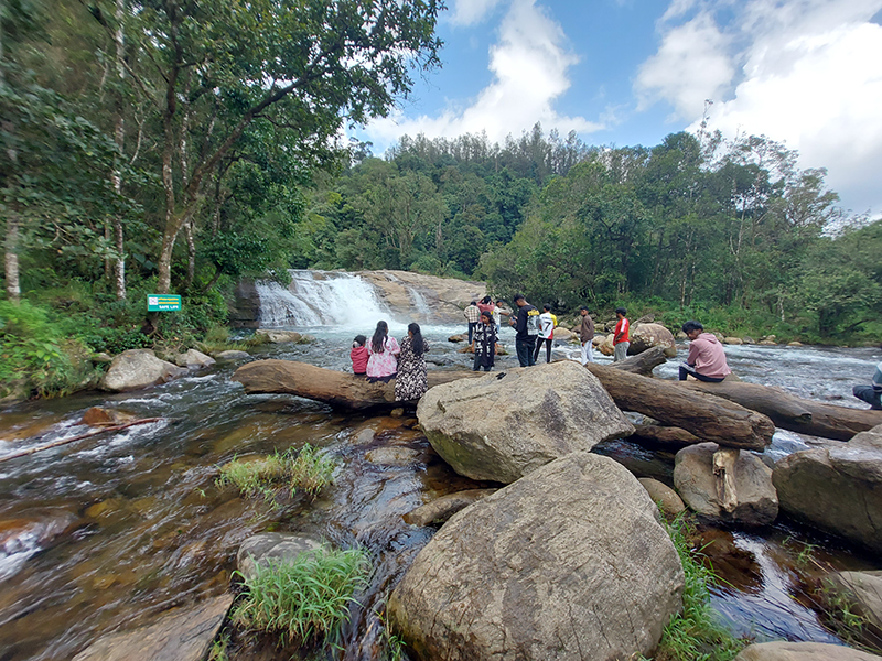 Tourists sitting near Chinnakallar Falls in Valparai enjoying scenic waterfall view